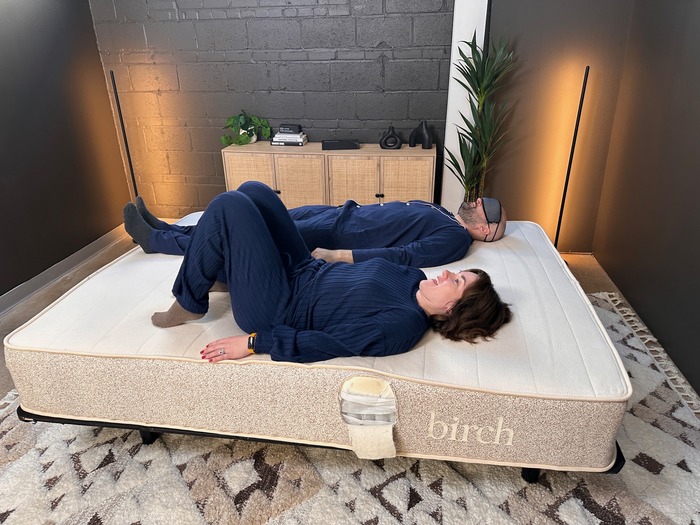 A man and a woman lying next to each other on the Birch Natural mattress. The man is wearing a sleep mask over his eyes.