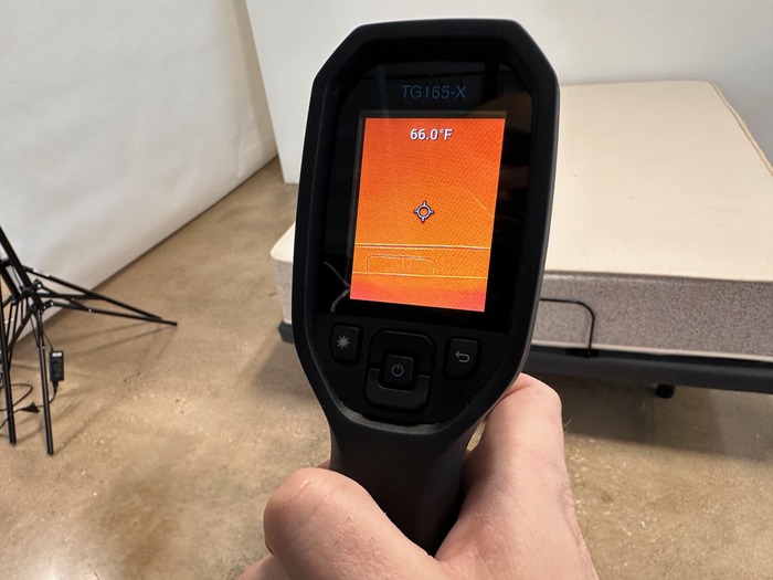 A closeup of a hand holding a thermal temperature gun and pointing it at a mattress.