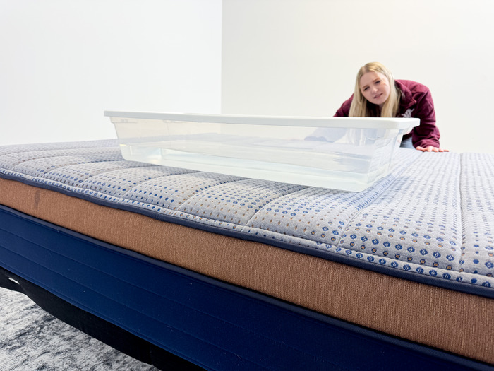 A woman looking at a plastic bin full of water on top of a mattress.