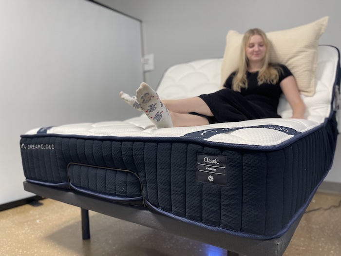 A woman sitting on the DreamCloud mattress, which is propped up at an incline on an adjustable base.