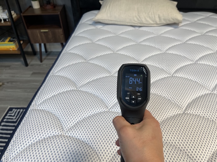 A closeup of someone using a thermal gun to take the temperature of the DreamCloud Premier Hybrid after someone has rested on it for 5 minutes. The screen reads 84.4 degrees.