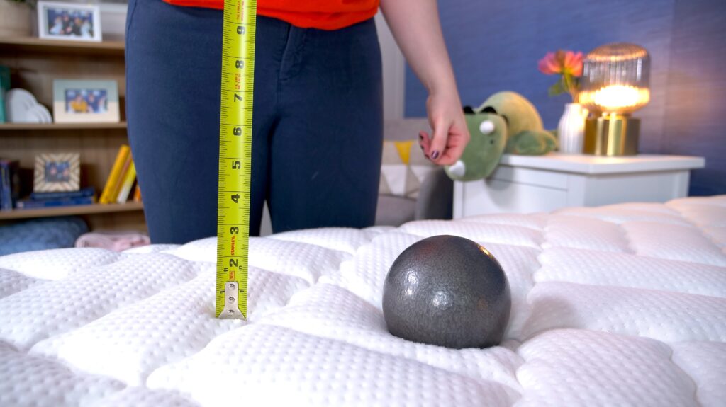 A woman standing over the Titan Plus. A steel ball has been dropped onto the bed and she's measuring its sinkage with a tape measure.