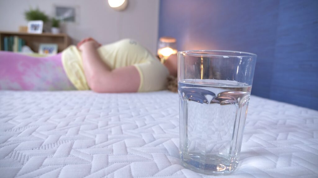 A person sleeps on a mattress next to a glass of water