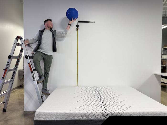 A man stands on a ladder and holds a 25-pound steel ball over the Nectar Luxe mattress.