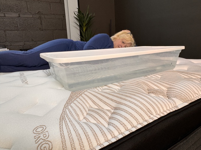 A woman lying next to a plastic bin full of water on the Nolah Evolution mattress.