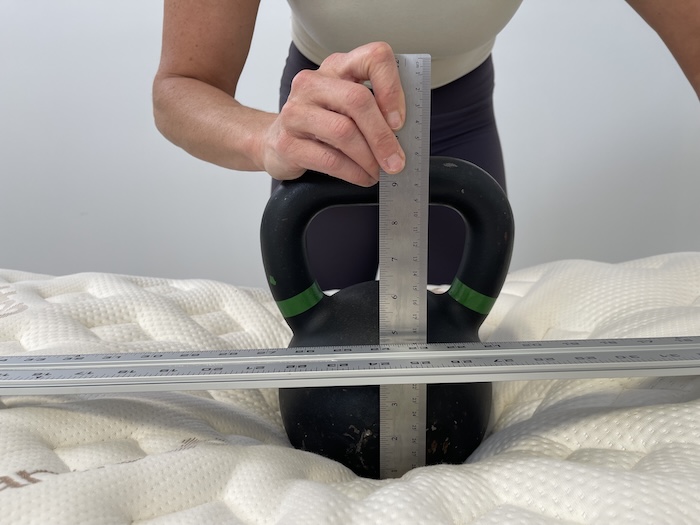 A closeup of a kettlebell resting on the Saatva Rx mattress. A woman measures its sinkage.