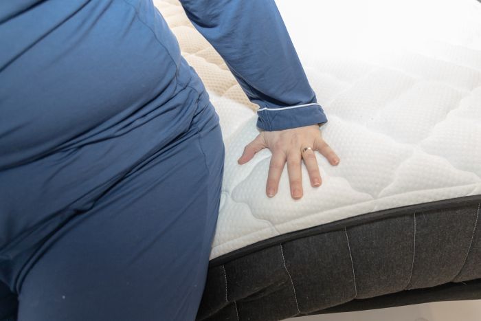 A woman sits on the edge of the Titan Plus mattress