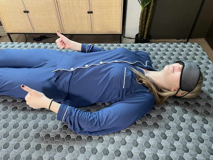 A woman lying on her back on the firm side of the Layla mattress while wearing an eye mask. She's giving a thumbs up to indicate that she can feel her partner moving next to her.