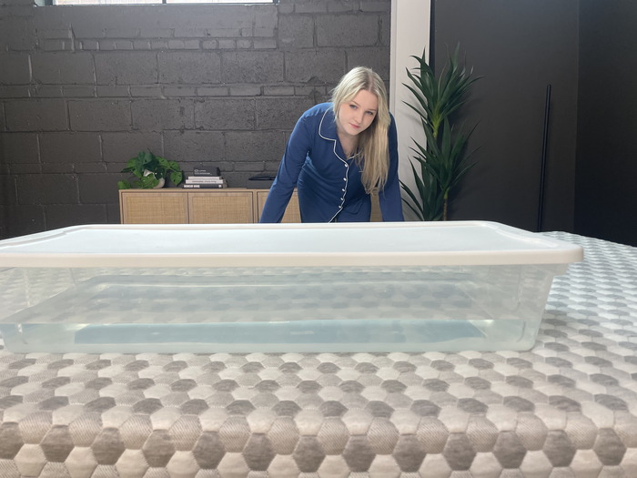 A woman standing and looking at a bin full of water on the Layla mattress.