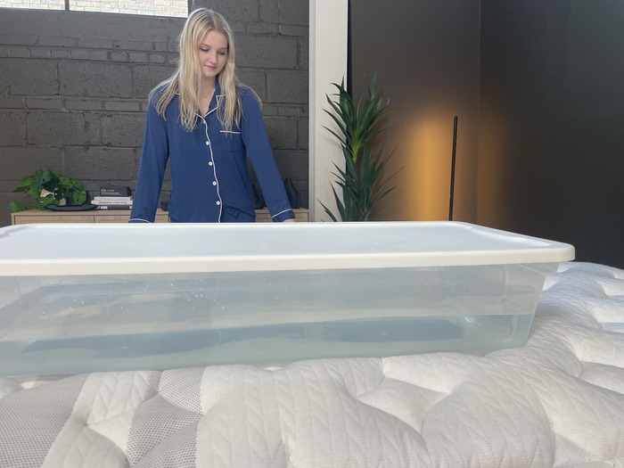 A woman staring at a plastic bin full of water on the Leesa Sapira Chill Hybrid.