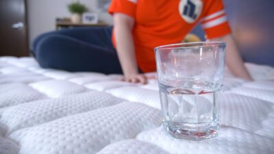 A woman sitting on the Brooklyn Bedding Titan Plus mattress next to a full water glass.